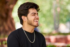 Smiling young indian man portrait in black t shirt and silver neck chain outdoor green public park